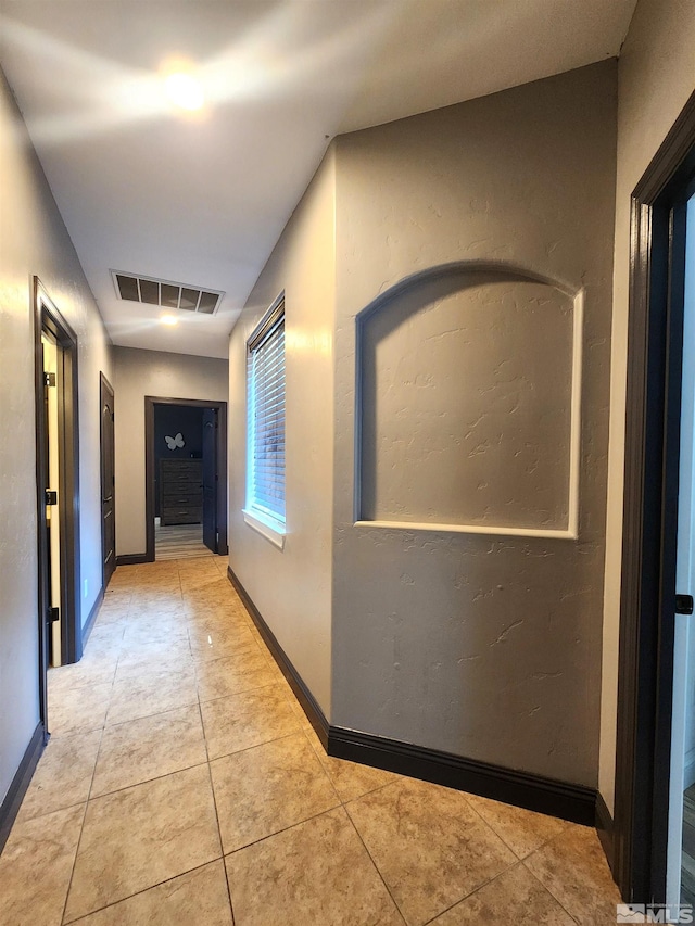 hallway featuring light tile patterned flooring, visible vents, and baseboards