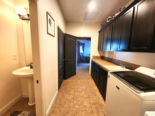 kitchen with light tile patterned floors, a sink, washer / dryer, and baseboards