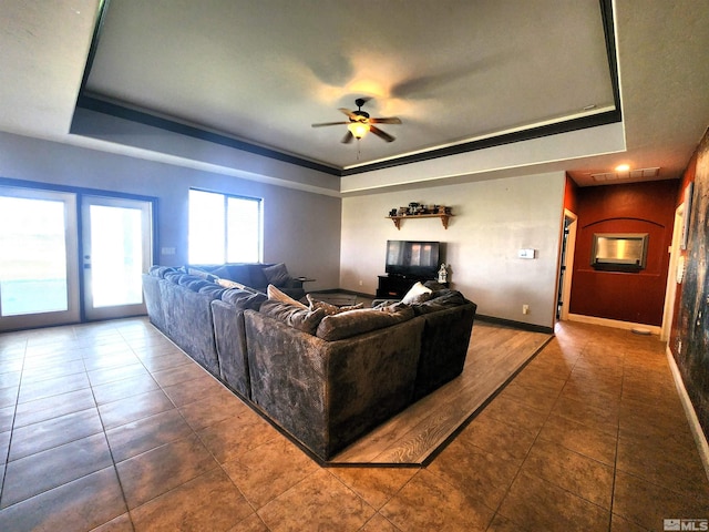 tiled living room featuring baseboards, a tray ceiling, and ceiling fan