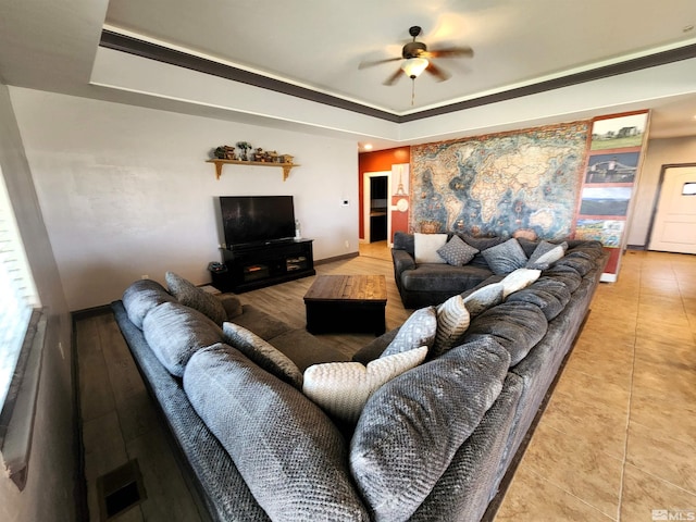 living room featuring baseboards, a raised ceiling, a ceiling fan, and tile patterned floors