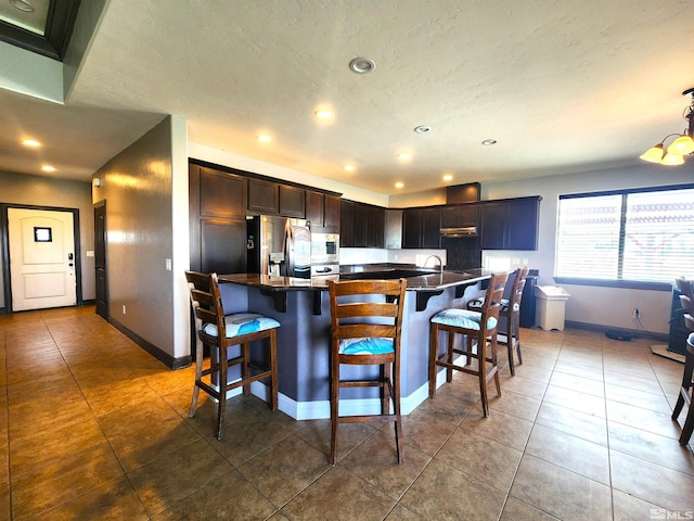 kitchen featuring a breakfast bar, dark tile patterned floors, baseboards, a large island, and stainless steel fridge with ice dispenser