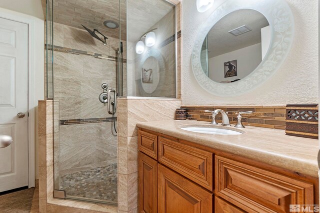 bathroom with a textured ceiling, tile walls, an enclosed shower, vanity, and decorative backsplash