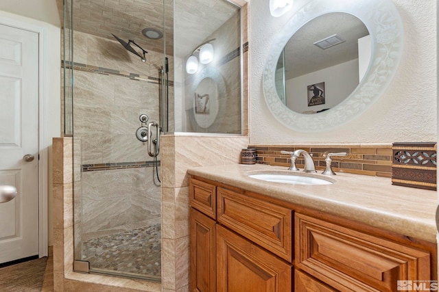 full bath with vanity, backsplash, a shower stall, and visible vents