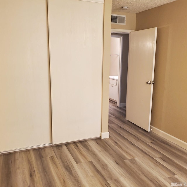 unfurnished bedroom featuring a closet, a textured ceiling, and light hardwood / wood-style flooring