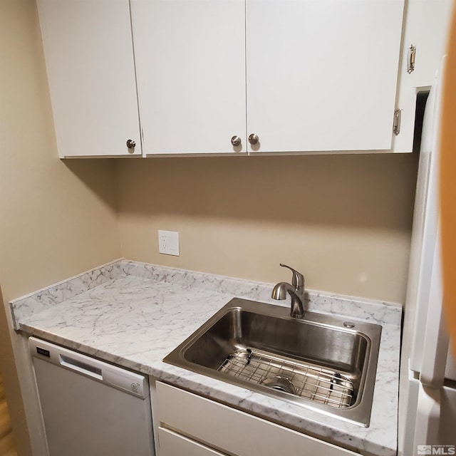 kitchen featuring light stone counters, white cabinets, sink, and dishwasher