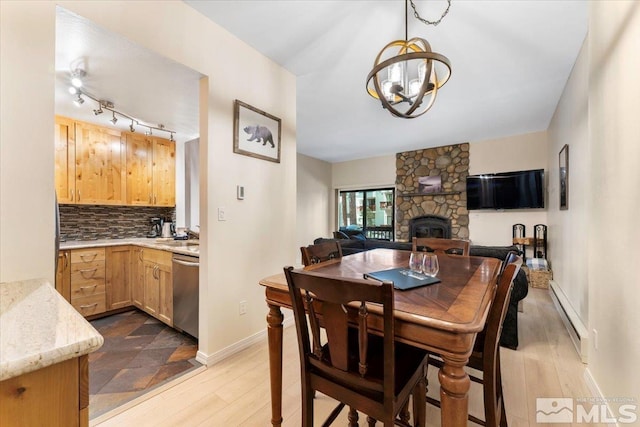 dining room with light wood-style floors, a baseboard radiator, a fireplace, and a notable chandelier