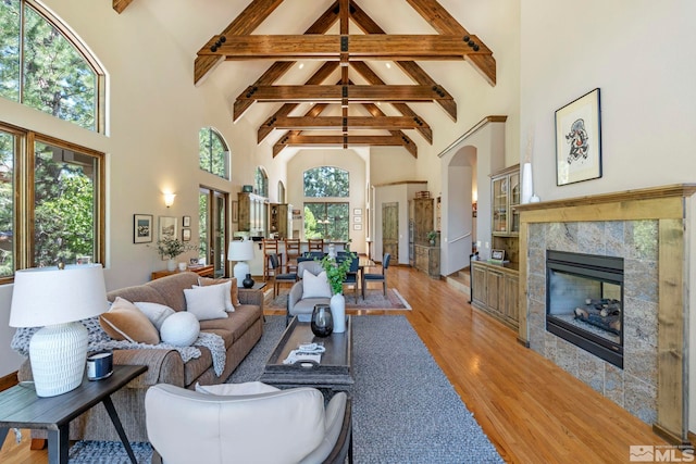 living room featuring light hardwood / wood-style floors, a tiled fireplace, a healthy amount of sunlight, and a towering ceiling