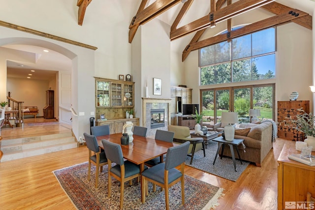 dining room featuring beamed ceiling, high vaulted ceiling, light hardwood / wood-style flooring, and a high end fireplace