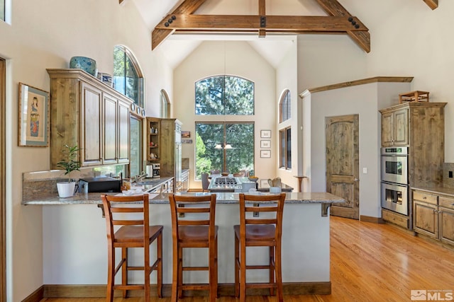 kitchen featuring high vaulted ceiling, plenty of natural light, stainless steel double oven, and beam ceiling