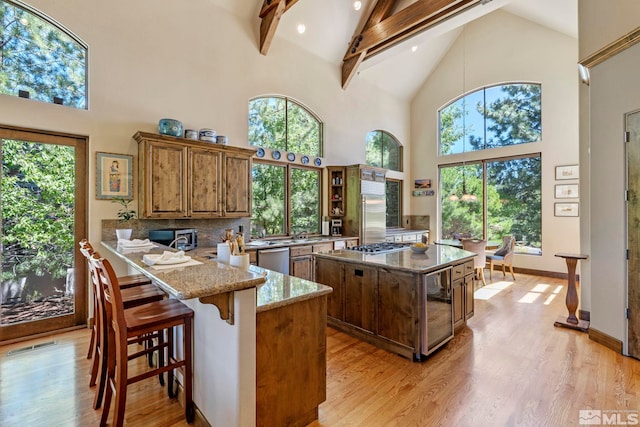 kitchen featuring beam ceiling, light wood-type flooring, a wealth of natural light, high vaulted ceiling, and a kitchen island