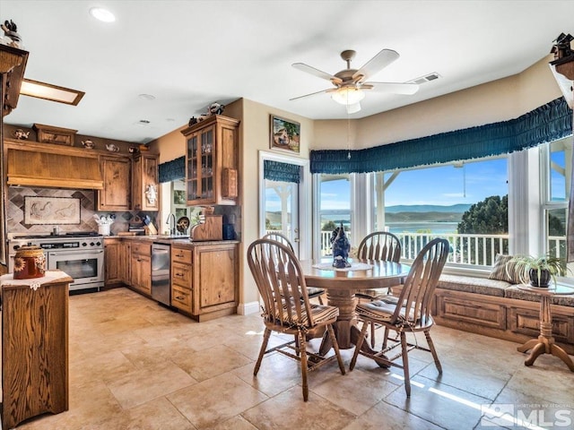 kitchen featuring brown cabinets, backsplash, glass insert cabinets, appliances with stainless steel finishes, and a ceiling fan