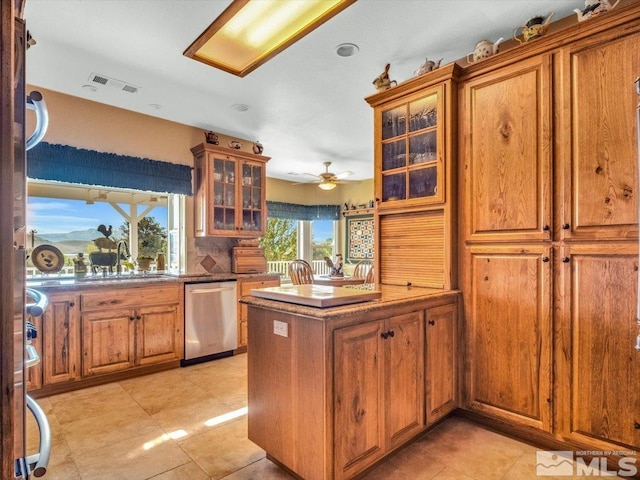 kitchen with a peninsula, a sink, dishwasher, brown cabinetry, and glass insert cabinets