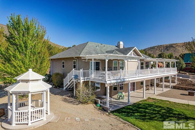 back of house featuring a patio, a chimney, a deck with mountain view, a gazebo, and a yard