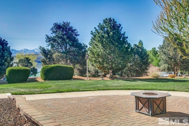 view of community featuring an outdoor fire pit, a patio area, a mountain view, and a lawn