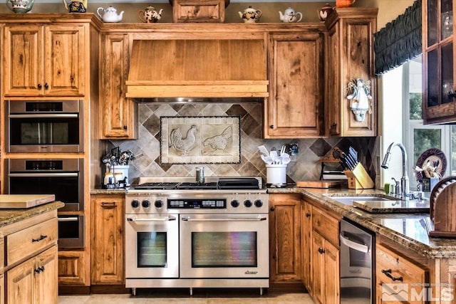 kitchen with appliances with stainless steel finishes, dark stone countertops, a sink, and brown cabinets