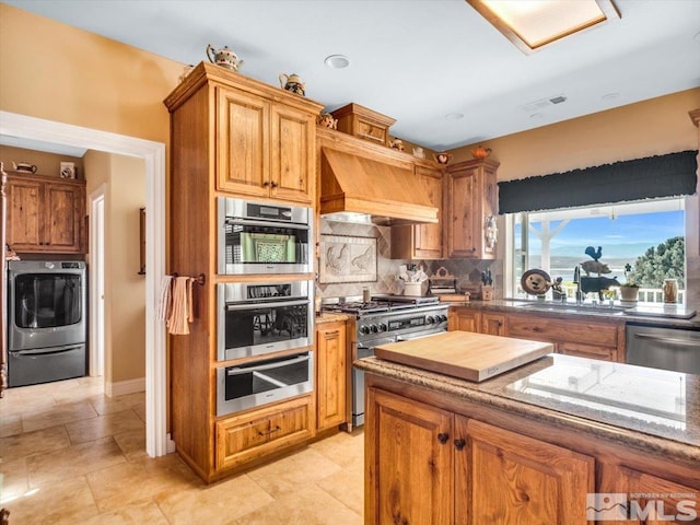 kitchen with appliances with stainless steel finishes, washer / clothes dryer, custom exhaust hood, a sink, and a warming drawer