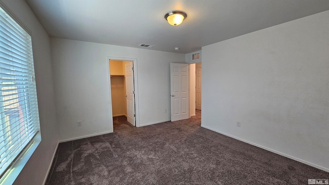 unfurnished bedroom with dark colored carpet, a closet, and a spacious closet