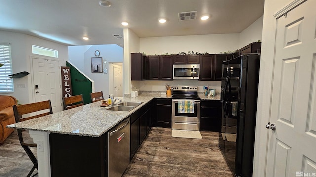 kitchen with a kitchen bar, appliances with stainless steel finishes, kitchen peninsula, dark wood-type flooring, and sink