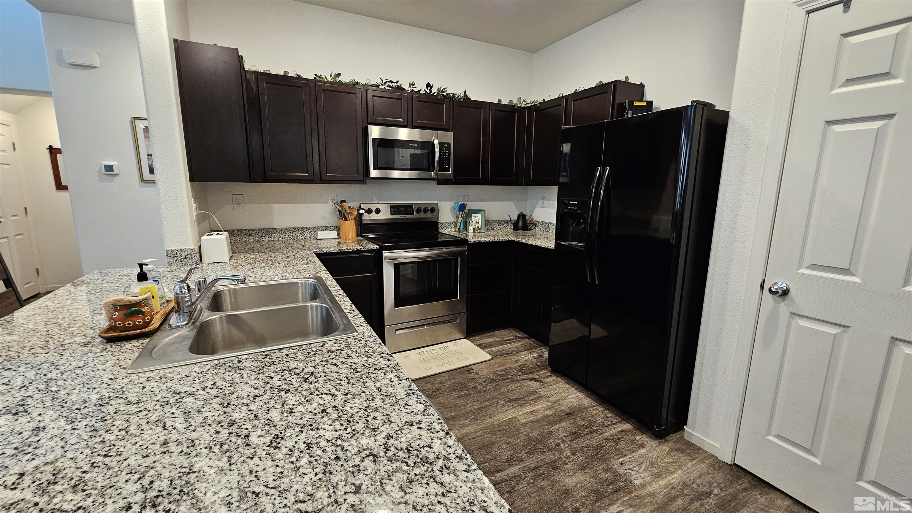 kitchen featuring dark hardwood / wood-style floors, appliances with stainless steel finishes, dark brown cabinets, sink, and light stone counters