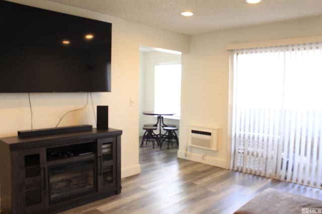 living area with recessed lighting, a textured ceiling, wood finished floors, a wall mounted air conditioner, and baseboards