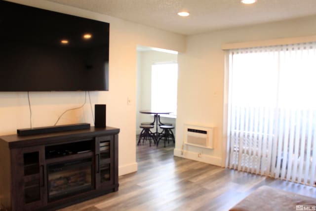 living area with recessed lighting, a wall mounted AC, a textured ceiling, wood finished floors, and baseboards