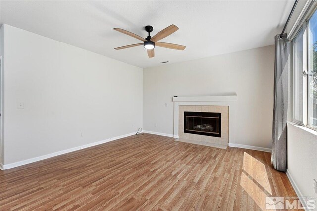 unfurnished living room with ceiling fan, light wood-type flooring, a tiled fireplace, and plenty of natural light