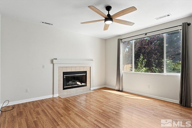 unfurnished living room featuring baseboards, visible vents, a tiled fireplace, and wood finished floors