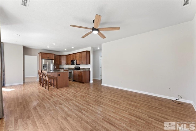 kitchen with appliances with stainless steel finishes, a breakfast bar area, light wood-type flooring, ceiling fan, and a center island