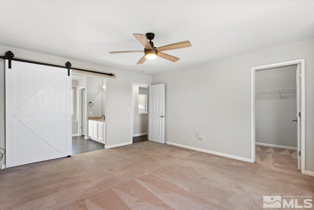 unfurnished bedroom with carpet floors, a walk in closet, a closet, a barn door, and baseboards