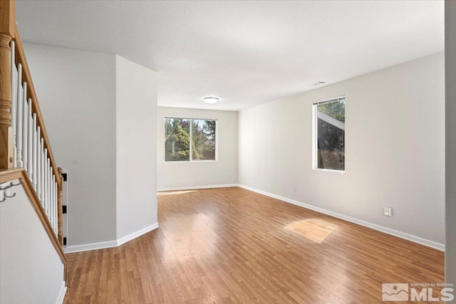 unfurnished room featuring visible vents, stairway, a textured ceiling, light wood-type flooring, and baseboards