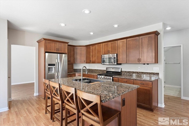 kitchen with an island with sink, light wood-style flooring, a breakfast bar, stainless steel appliances, and a sink