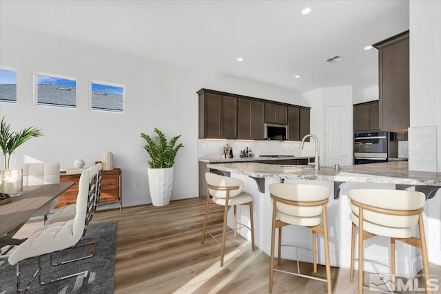 kitchen featuring dark brown cabinets, sink, backsplash, and light hardwood / wood-style flooring