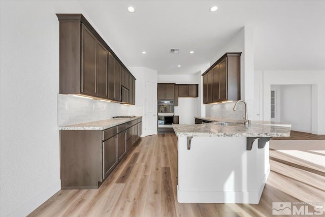 kitchen featuring multiple ovens, tasteful backsplash, sink, a kitchen breakfast bar, and light wood-type flooring