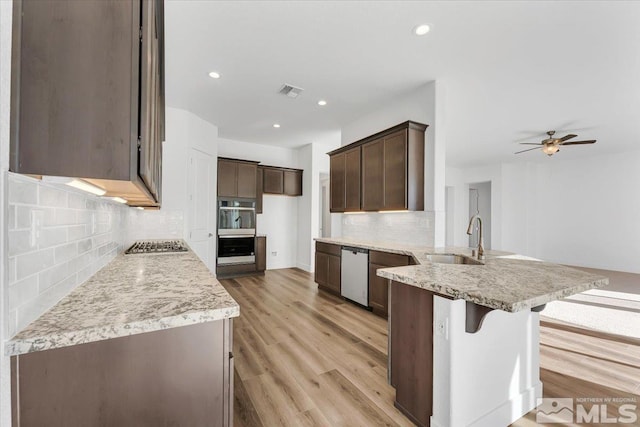 kitchen featuring sink, tasteful backsplash, light wood-type flooring, appliances with stainless steel finishes, and kitchen peninsula