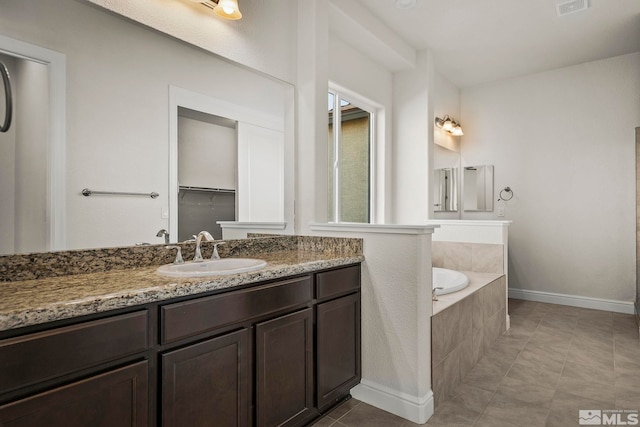 bathroom with tile patterned flooring, vanity, and a relaxing tiled tub