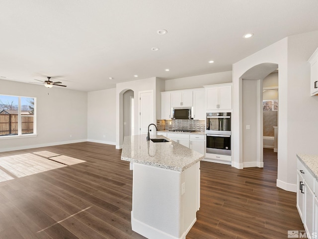 kitchen with arched walkways, stainless steel appliances, an island with sink, and a sink