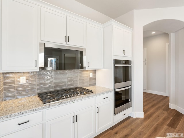 kitchen with arched walkways, white cabinets, light stone counters, double wall oven, and stainless steel gas stovetop