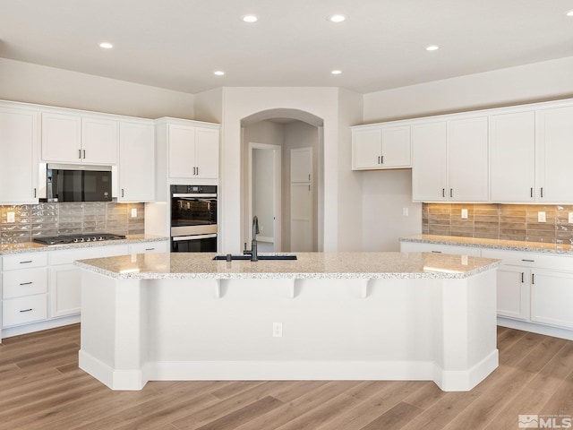 kitchen with an island with sink, a sink, white cabinets, and dobule oven black