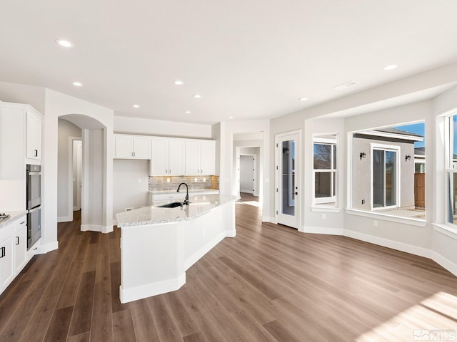 kitchen with arched walkways, white cabinets, a sink, and an island with sink