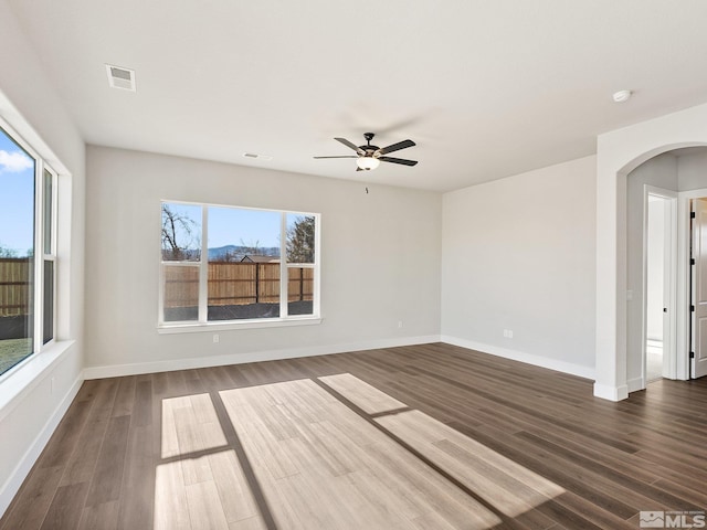 spare room featuring arched walkways, dark wood-type flooring, visible vents, and baseboards