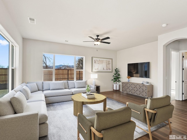 living area with ceiling fan, visible vents, arched walkways, and wood finished floors