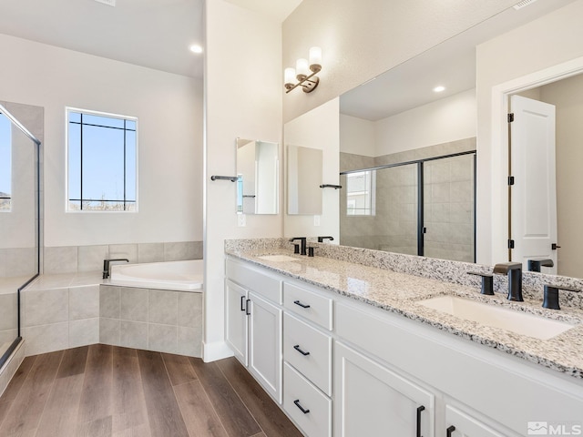 full bathroom with double vanity, a sink, a bath, and wood finished floors