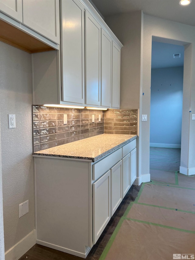 kitchen with light stone counters, visible vents, baseboards, white cabinets, and backsplash