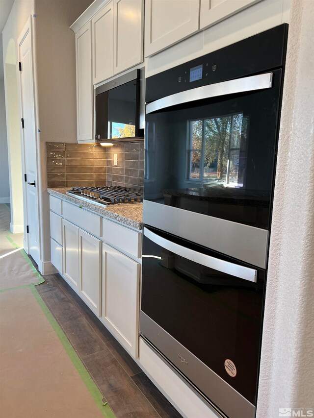 kitchen with appliances with stainless steel finishes, tasteful backsplash, light stone counters, dark wood-type flooring, and white cabinetry