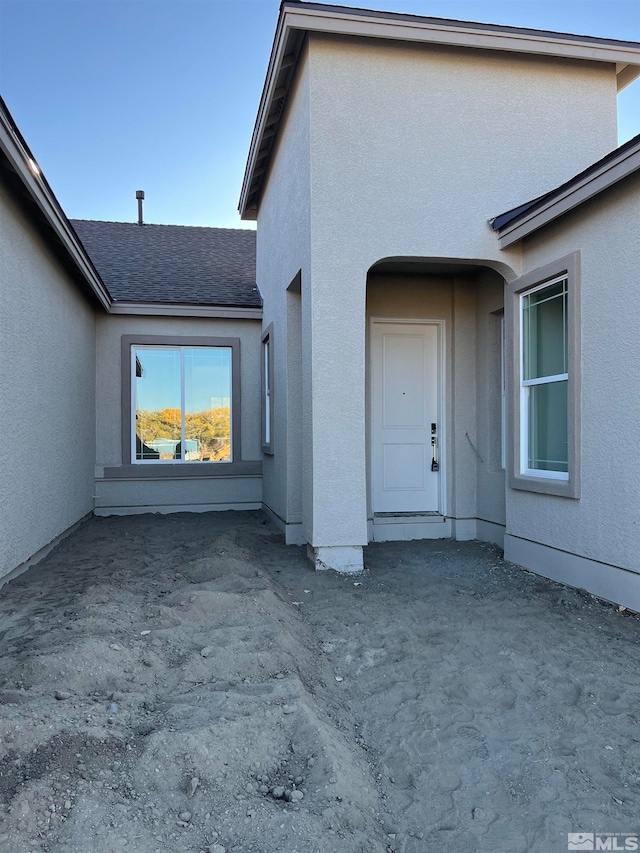 entrance to property featuring a shingled roof and stucco siding