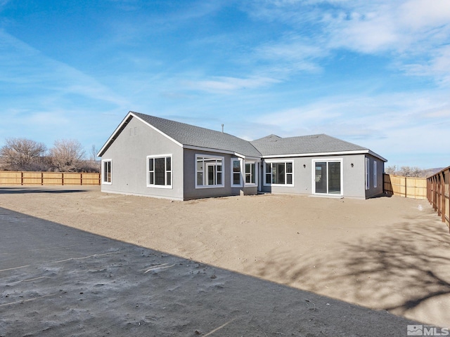 rear view of property featuring a shingled roof, a fenced backyard, and stucco siding