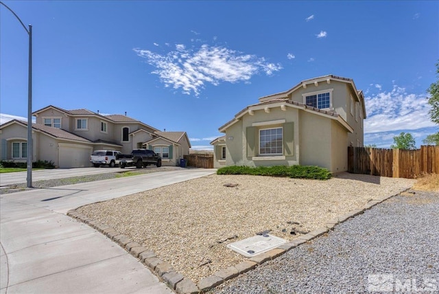 view of front of house featuring driveway, a residential view, fence, and stucco siding