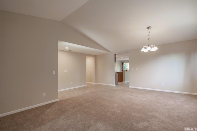 carpeted spare room featuring a notable chandelier and vaulted ceiling