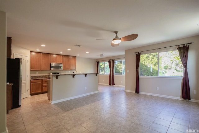 kitchen featuring ceiling fan, light tile patterned flooring, a breakfast bar, and black fridge