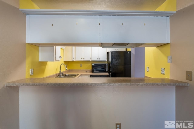 kitchen featuring white cabinets, sink, kitchen peninsula, and black fridge